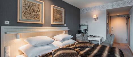 Habitación de hotel moderna con una cama grande, dos obras de arte enmarcadas, un escritorio con silla y una mesita con espejo y objetos decorativos.