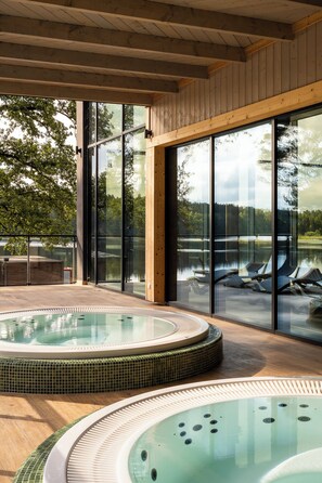 A modern spa area with two hot tubs, large windows, and a view of a lake.