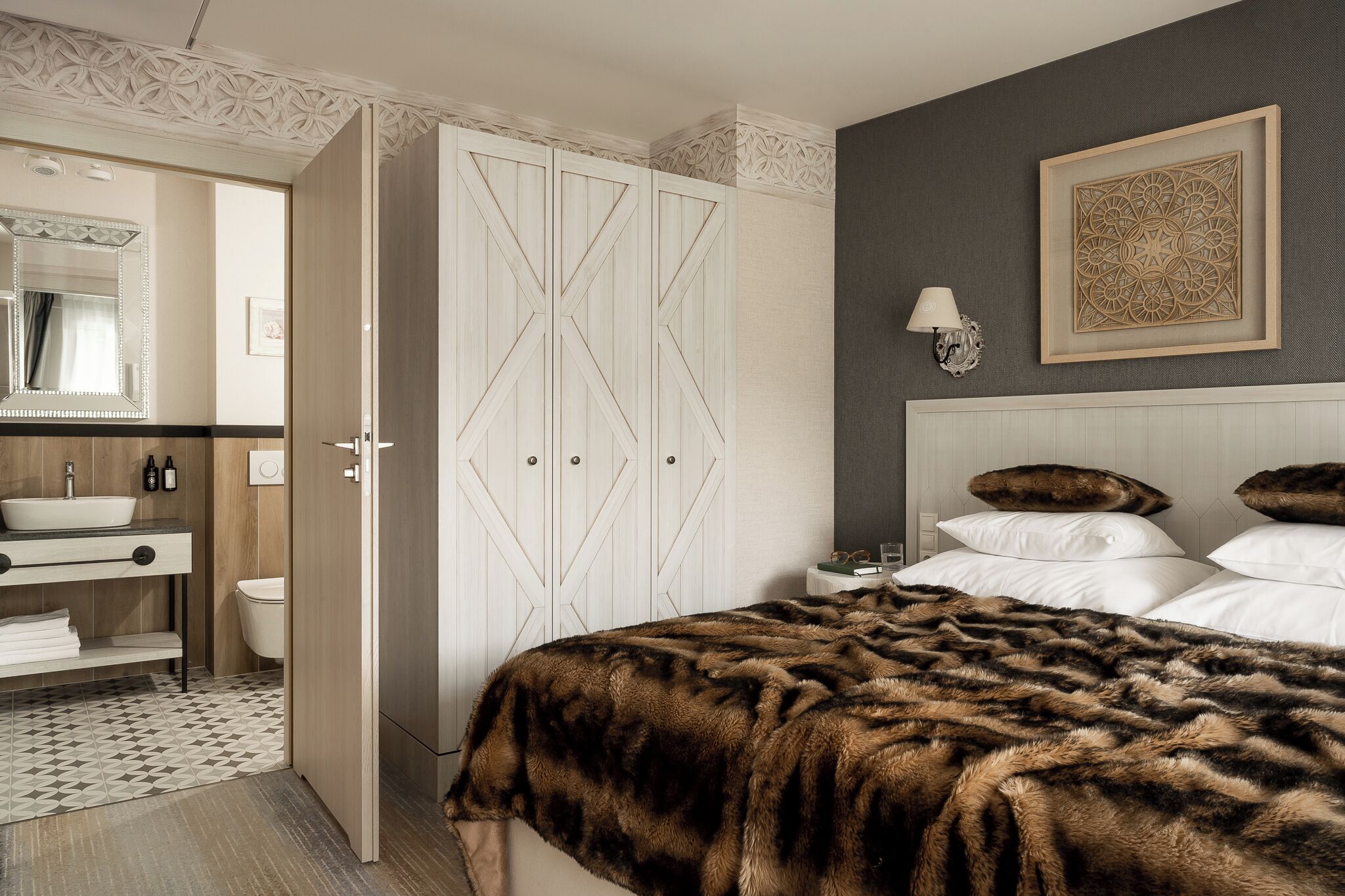 A bedroom with a large bed, a nightstand, a dresser, a mirror, and a wardrobe.