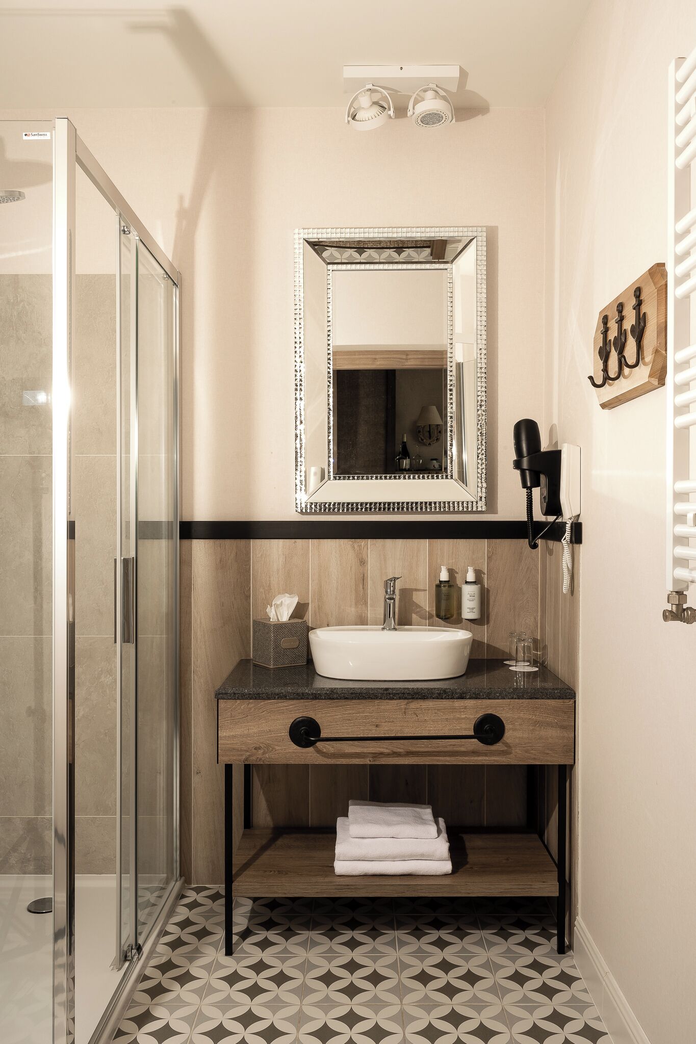 A bathroom with a glass shower enclosure, a wooden vanity with a sink, a mirror, and a towel rack.