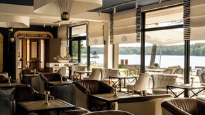 Un restaurante con terraza, amplios ventanales y vistas a un lago.