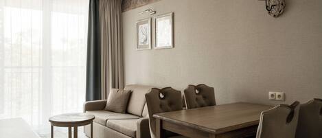 Habitación de hotel con sofá, mesa de comedor, una mesita redonda, lámpara de pared y dos cuadros enmarcados.