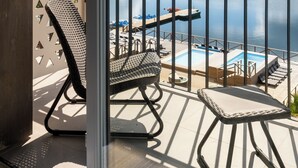 Un balcón con vistas a un lago, una piscina y sillones de descanso.