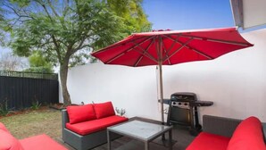 A patio with a red umbrella, a grill, and red furniture. - Bayside Home Away From Home (Brighton)