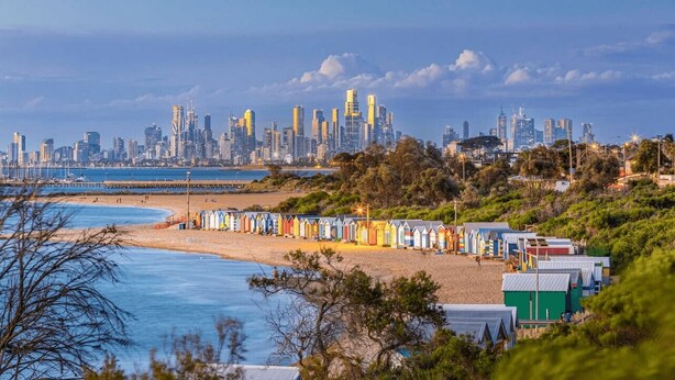 A beach with colorful beach huts and a city skyline in the background. - Bayside Home Away From Home (Brighton)