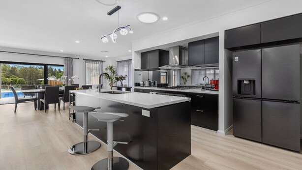 A modern kitchen with a large island, dark cabinetry, and stainless steel appliances.