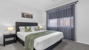 A neatly arranged bedroom with a bed, two bedside tables, a lamp, a decorative pillow, a throw blanket, and a window with curtains.