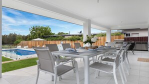 A spacious outdoor dining area with a view of a swimming pool and a backyard.