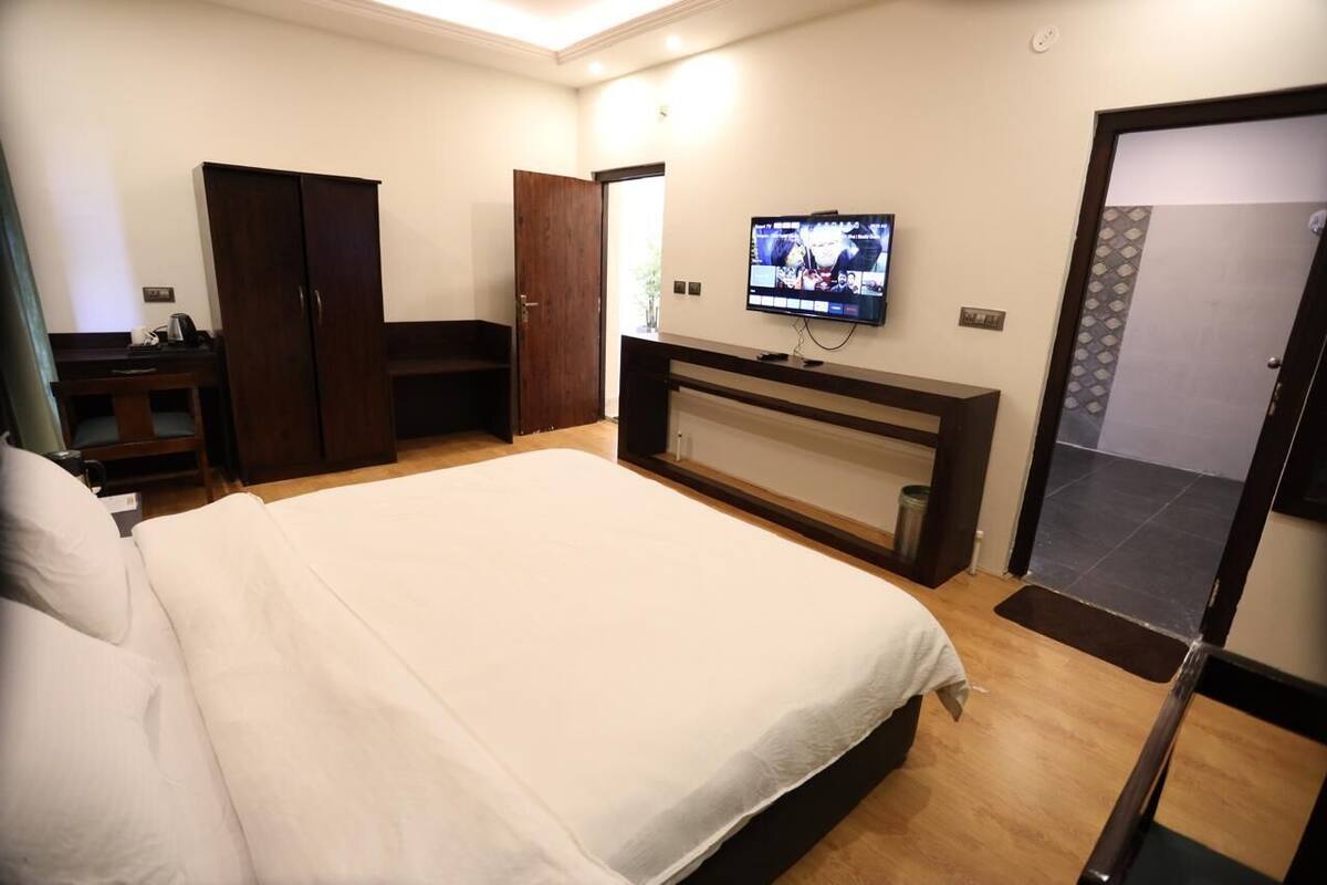 A hotel room with a large bed, a TV mounted on the wall, a wardrobe, and a desk with a chair.