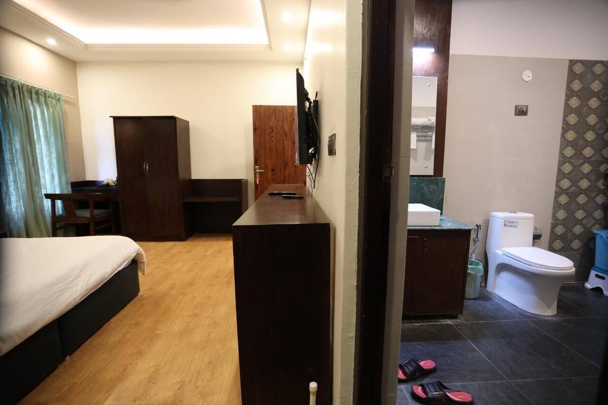 A hotel room with a bed, a desk, a wardrobe, a television, a bathroom with a toilet, and a sink.