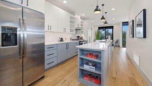 A modern kitchen with stainless steel appliances, grey cabinets, and a central island with storage shelves. - Atlas - Trailhead Mews - Optional BlakeSt Access (Bentonville)