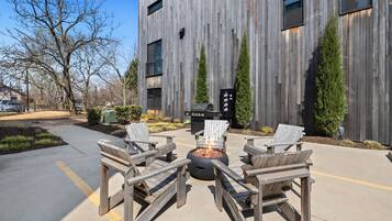 A modern building with a wooden facade, outdoor seating with chairs and a fire pit, and a barbecue grill.
