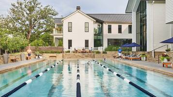 A swimming pool with lane dividers, surrounded by lounge chairs and umbrellas, with a building in the background.