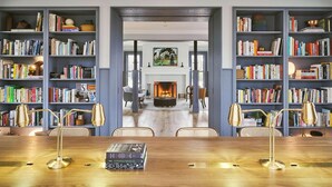Tilava huone, jossa on suuri puinen pöytä, kaksi tuolia ja täynnä kirjoja oleva kirjahylly. Taustalla näkyy takka, ja huoneen sisustus on moderni.