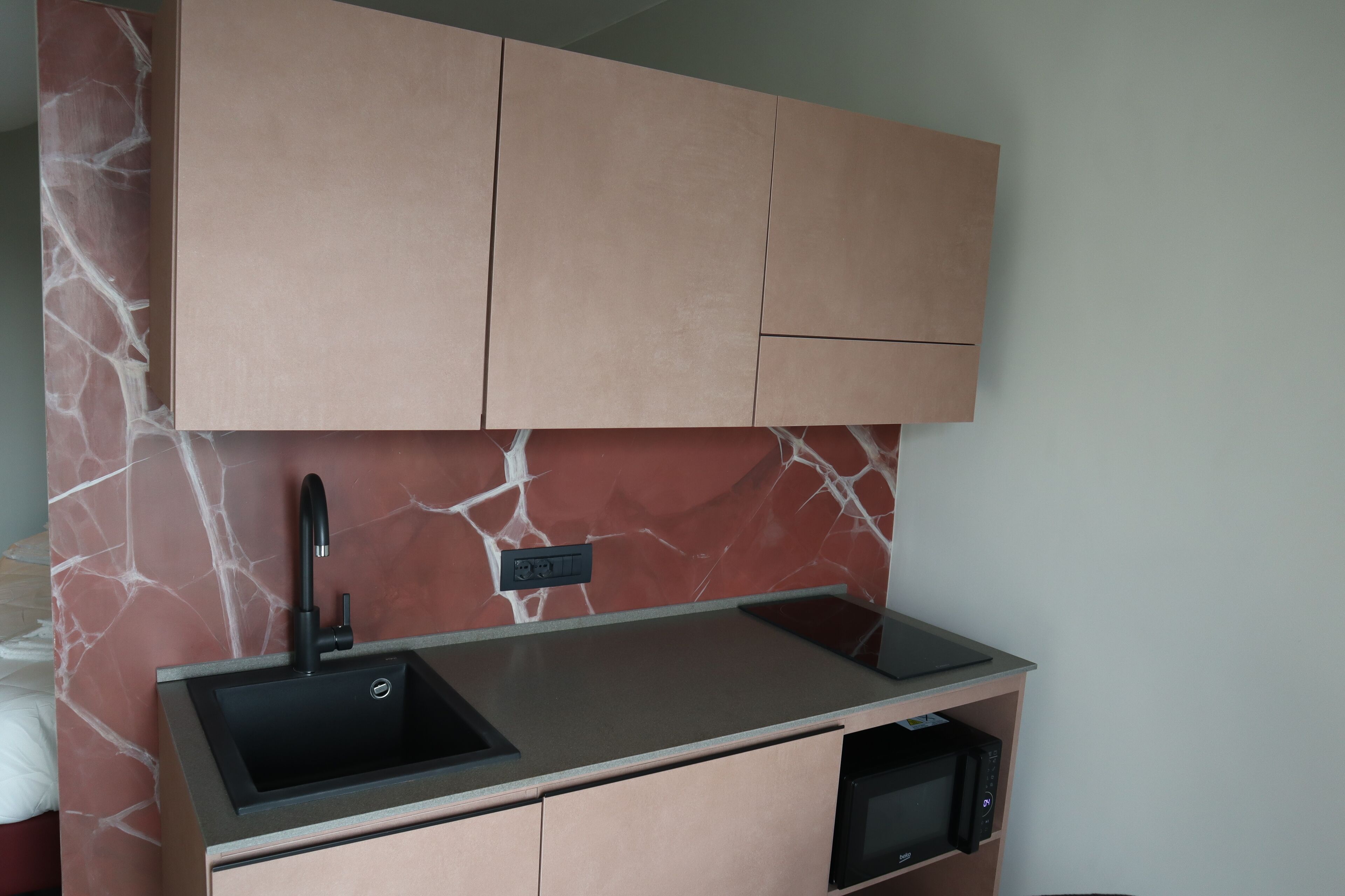 A compact kitchen with a marble backsplash, a black sink, and a microwave.