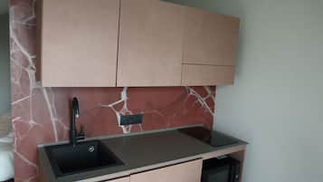 A compact kitchen with a marble backsplash, a black sink, and a microwave.