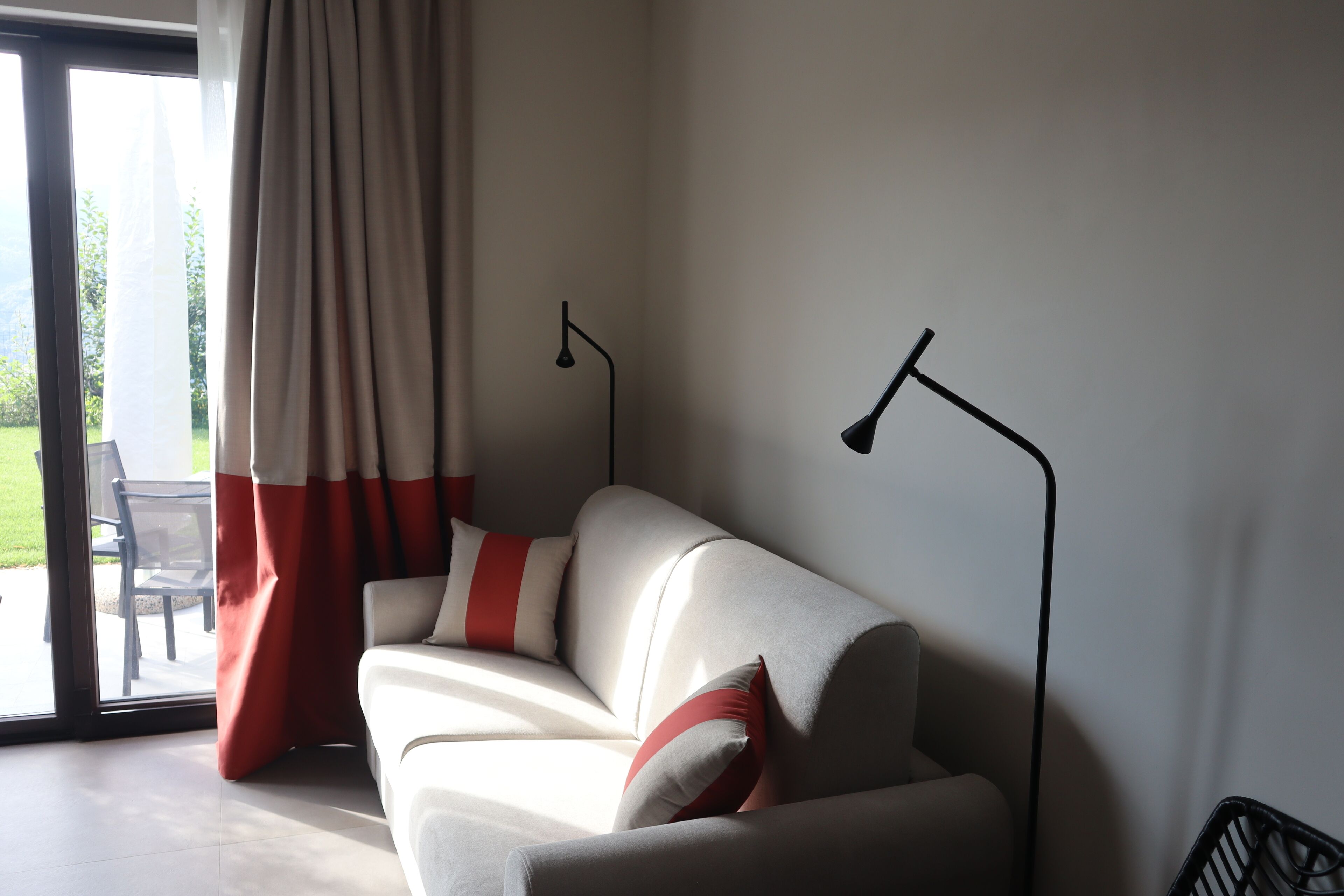A modern living room with a sofa, two floor lamps, and a sliding glass door leading to an outdoor area.