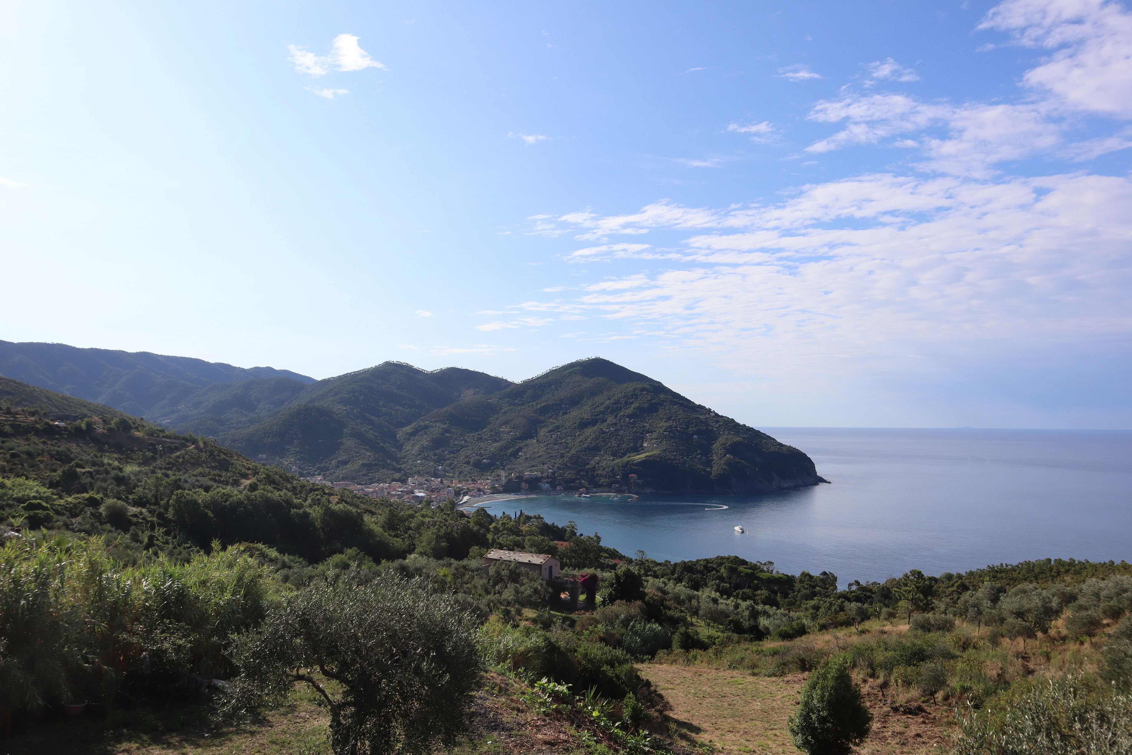 Paesaggio costiero con colline, un piccolo insediamento e cielo sereno.