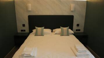 A neatly made bed with pillows and folded towels, two bedside tables, and wall-mounted light fixtures.