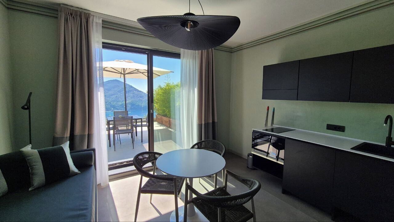 A modern hotel room with a balcony, a dining area, and a kitchenette.
