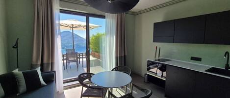 A modern hotel room with a balcony, a dining area, and a kitchenette.