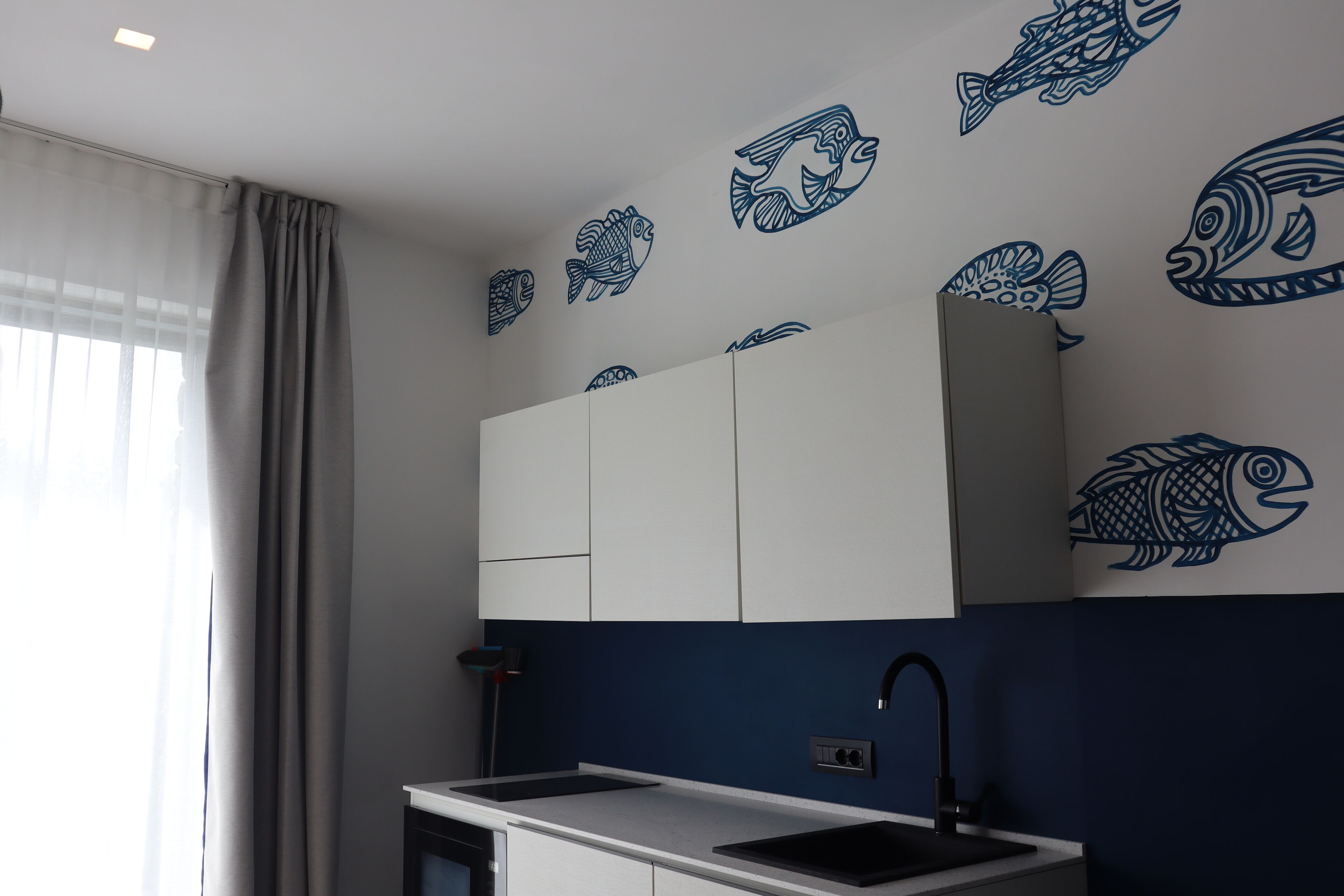 Une cuisine moderne avec des meubles blancs, un évier noir et des autocollants représentant des poissons bleus sur le mur.