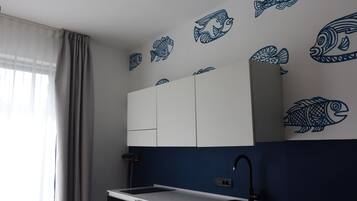 Une cuisine moderne avec des meubles blancs, un évier noir et des autocollants représentant des poissons bleus sur le mur.