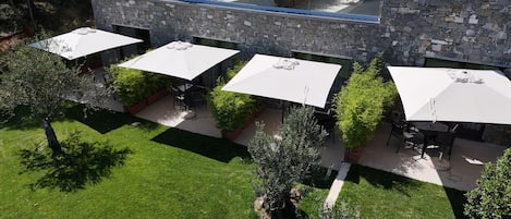 Un patio al aire libre con varias mesas y sombrillas, rodeado de muros de piedra y follaje.