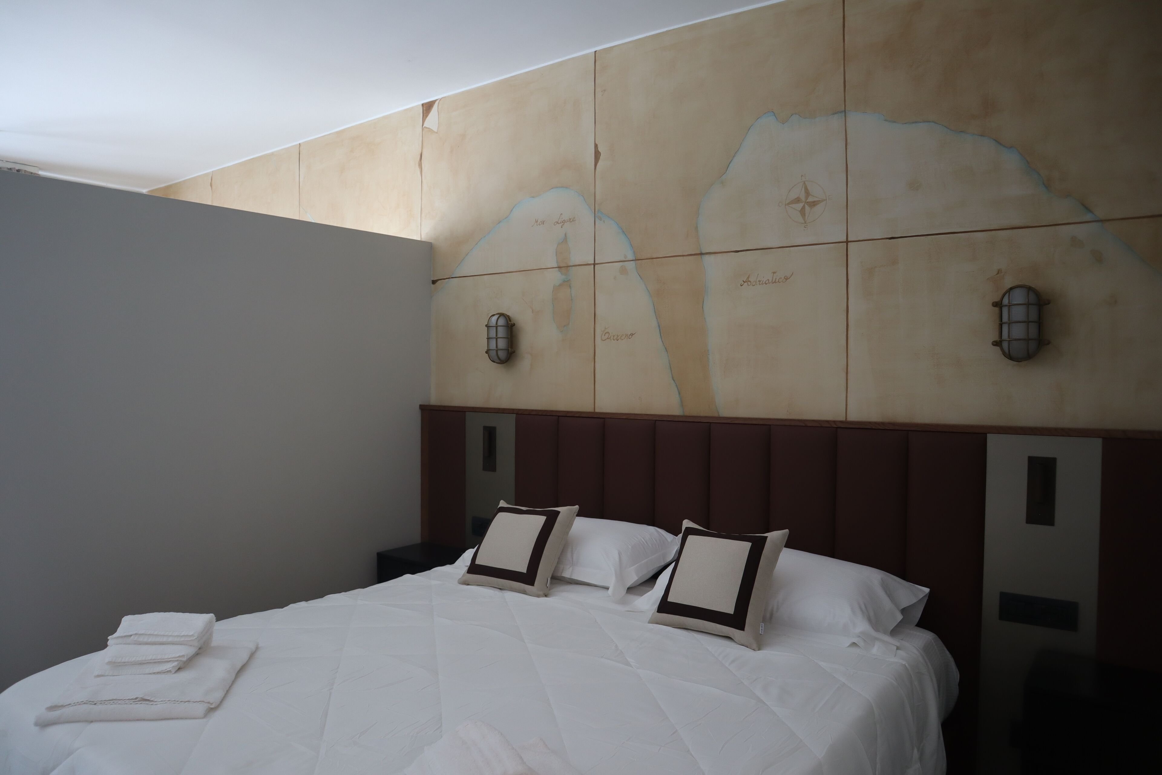 Une chambre d’hôtel avec un grand lit, une tête de lit ornée d’un motif de carte et deux appliques murales.