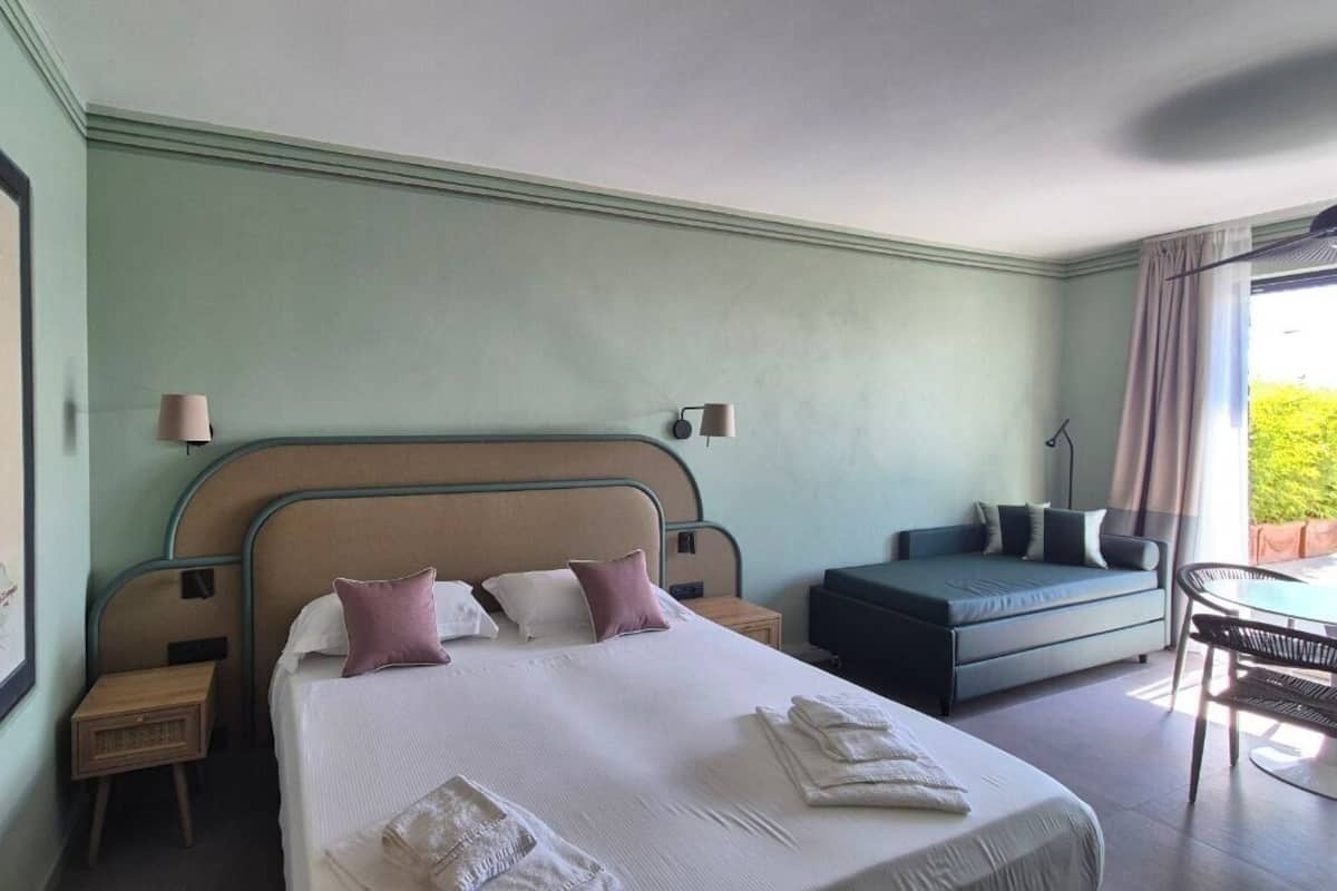 A hotel room with a large bed, a sofa, a small table, and a painting on the wall.