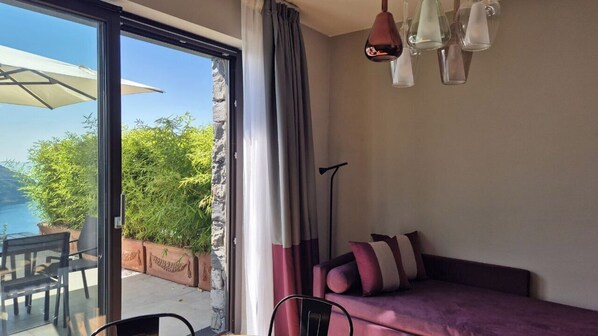A room with a purple sofa, a dining table with chairs, a large window with curtains, and a hanging light fixture. - La Giulia Suites like Home (Bonassola)