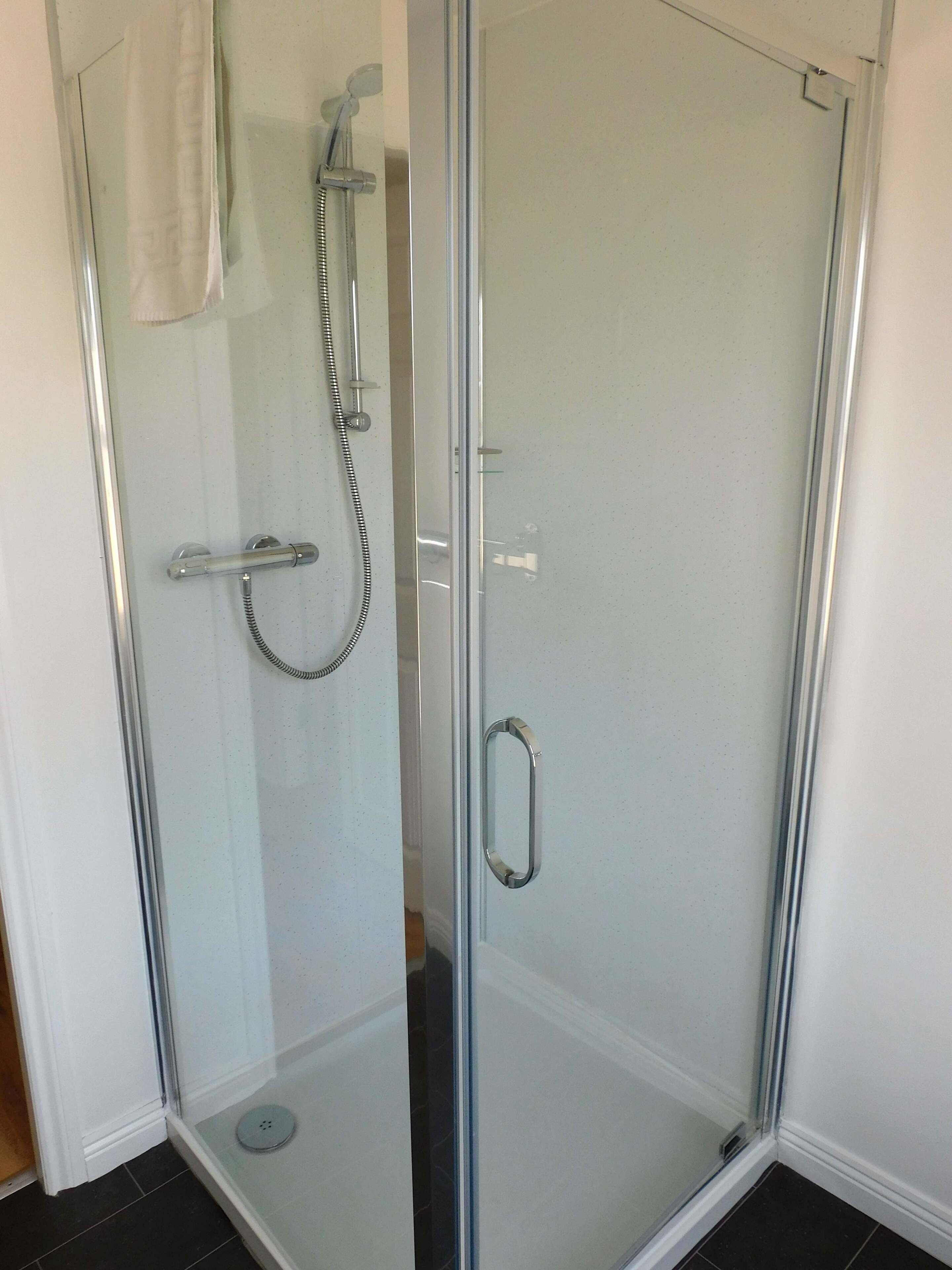 A glass-enclosed shower with a handheld showerhead and a handheld faucet.