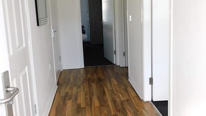 A hallway with wooden flooring, white walls, and a ceiling light fixture.