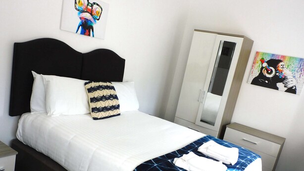 A neatly made bed with a white and blue patterned bedspread, a black headboard, and a decorative pillow.