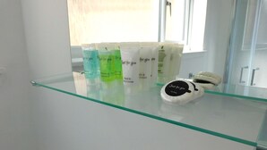 Un bagno con ripiano in vetro che espone diversi articoli da toilette, tra cui shampoo, balsamo e sapone.