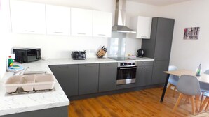 A modern kitchen with grey cabinets, a built-in oven, and a microwave. There's a dining area with a table and chairs.