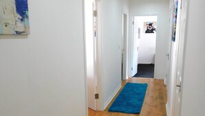 A hallway with wooden flooring, white walls, and a blue rug.