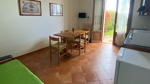 Ein Zimmer mit einem Bett, einem Esstisch mit Stühlen, einer Küchenzeile und einer Glastür, die zu einem Außenbereich führt.