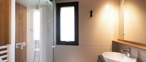 Un baño moderno con cabina de ducha de vidrio, lavamanos blanco y tocador de madera.