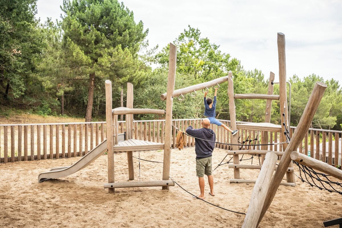 Una construcció de fusta per jugar amb tobogan i elements per escalar en una zona exterior de sorra.