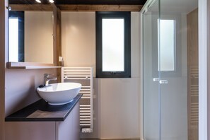 A modern bathroom with a white sink, a mirror, a window, and a glass shower enclosure. - Huttopia Arcachon  (Arcachon)