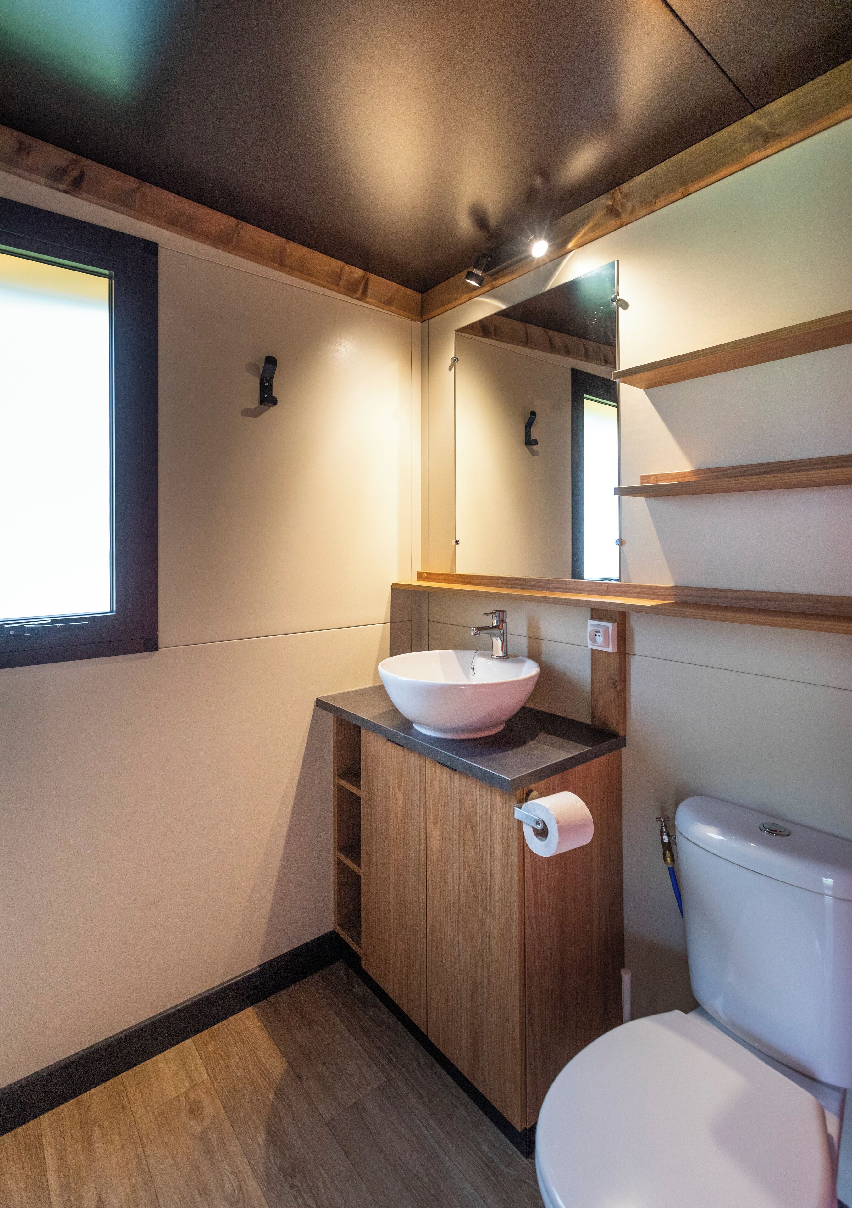 A compact bathroom with a wooden vanity, a white sink, and a toilet.