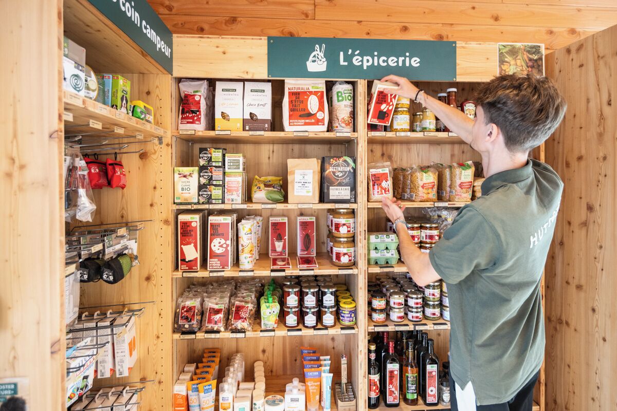 A person selecting items from a shelf in a store with wooden shelves and a variety of products.