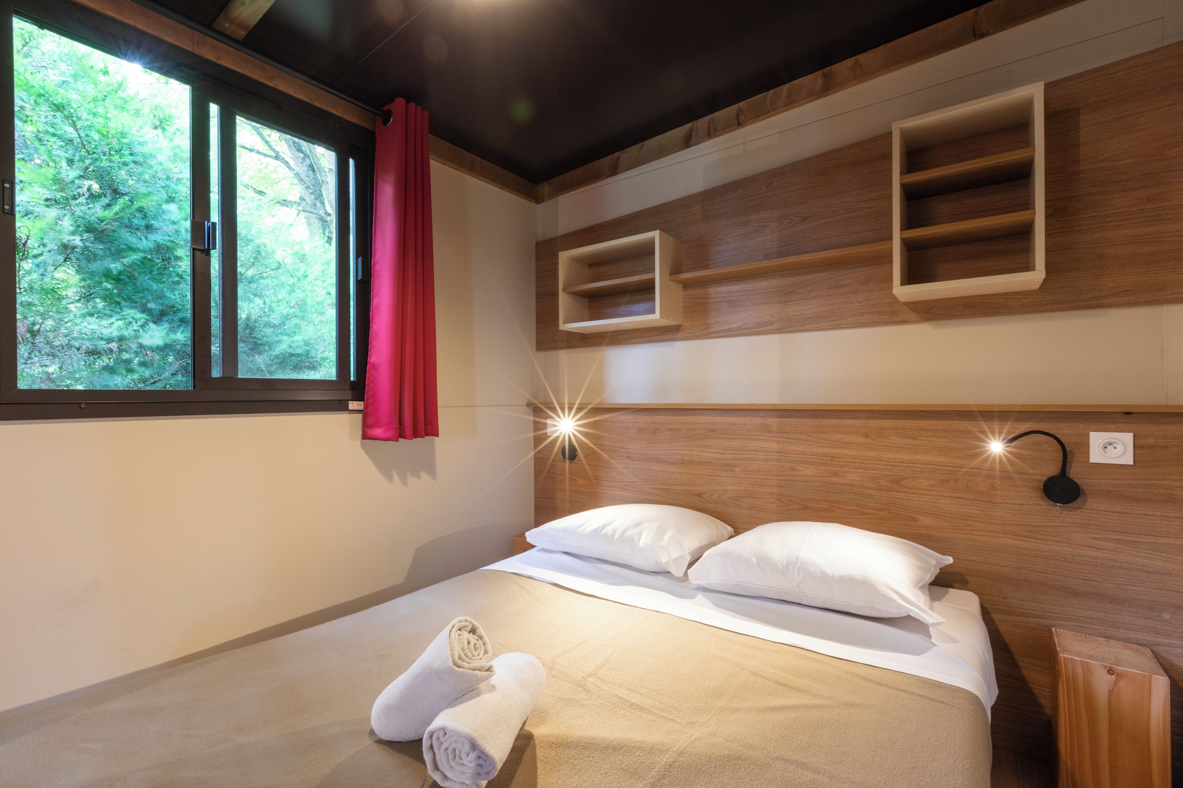 A modern bedroom with a large window, wooden headboard, and built-in shelves.