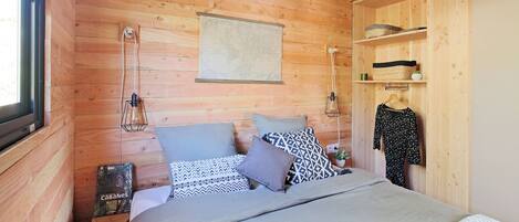 Una habitació de fusta acollidora amb un llit, almoines, una làmpada penjant i una estant amb objectes.