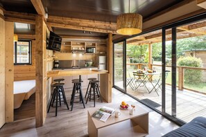 A modern kitchen with wooden accents, a dining area with a table and chairs, and a large sliding glass door leading to an outdoor patio. - Huttopia Arcachon  (Arcachon)
