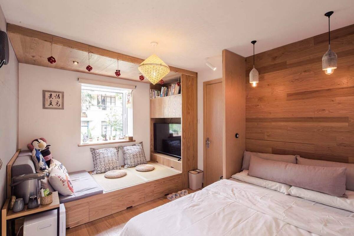 A bedroom with a built-in window seat, wooden wall paneling, a bed, and pendant lighting.