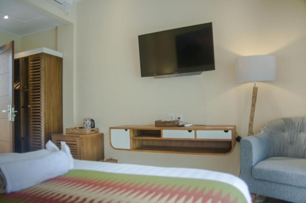 A hotel room with a bed, a television mounted on the wall, a wooden nightstand, a lamp, and a chair.