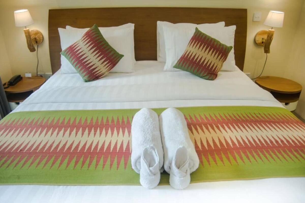 A hotel room with a large bed, two pillows, a bedside table with a lamp, and a pair of towels on the bed.