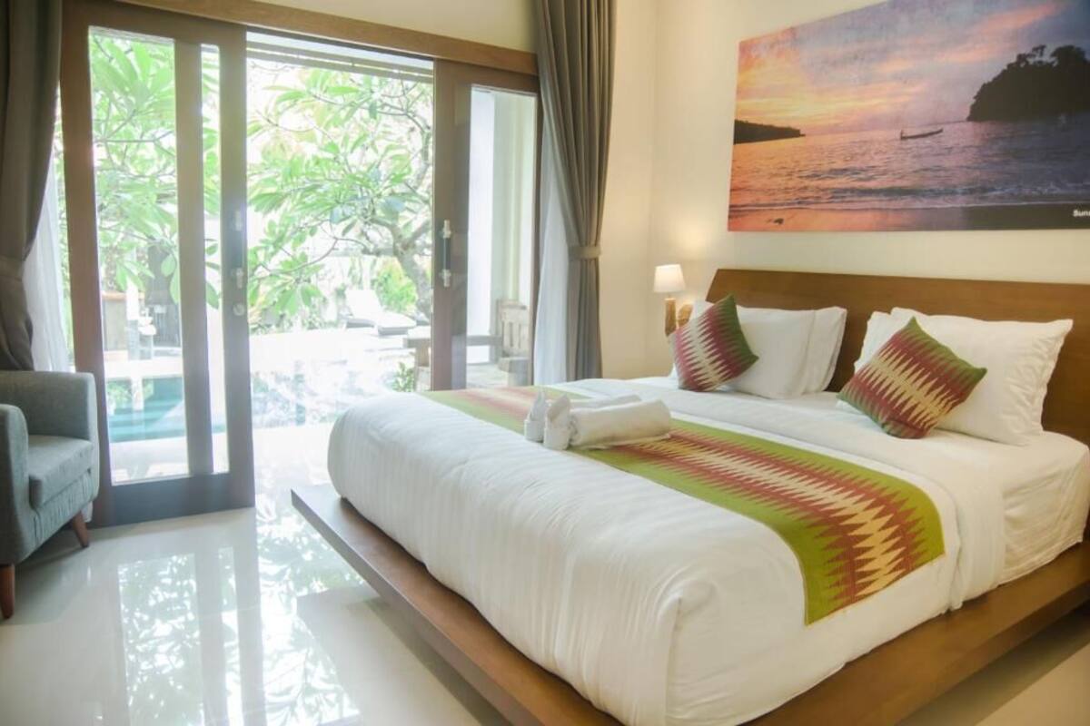 A hotel room with a large bed, a view of the outdoors, and a painting of a sunset over water.